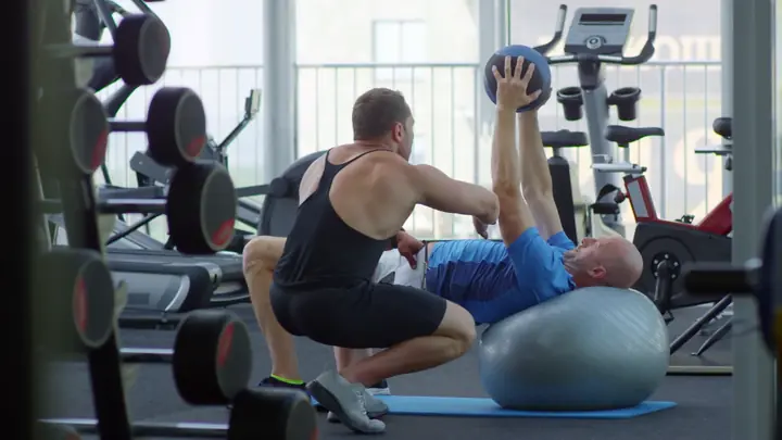 A trainer guiding a client on an exercise ball in a gym