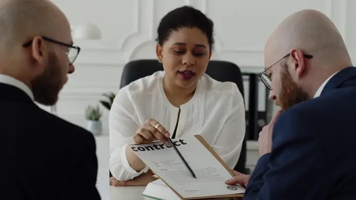 A woman and a man in suits reviewing a printed contract at a desk during a meeting