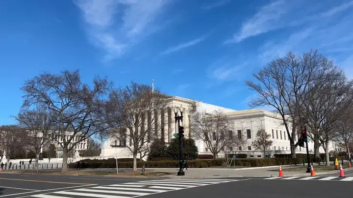 A large white courthouse building with columns seen across a street under a blue sky