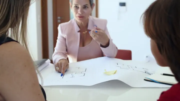 An agent going over a floor plan with two clients at a desk