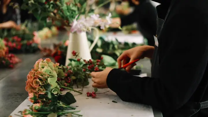 A florist trimming stems at a workbench of flowers