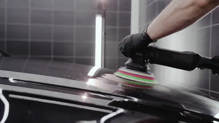 A detailer polishing a black car with a machine polisher