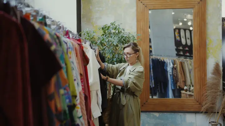 A boutique owner hanging clothes on a rack beside a mirror