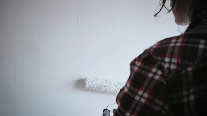 A painter rolling white paint onto a wall