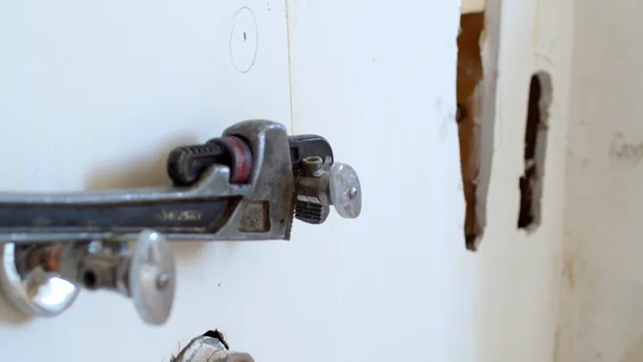 A pipe wrench gripping a valve fitting on a white wall